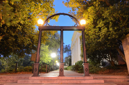The historic University of Georgia arch glows warmly under evening lights, framed by lush trees along a brick walkway near downtown Athens, GA, close to local retirement communities.