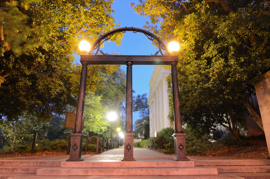 The historic University of Georgia arch glows warmly under evening lights, framed by lush trees along a brick walkway near downtown Athens, GA, close to local retirement communities.