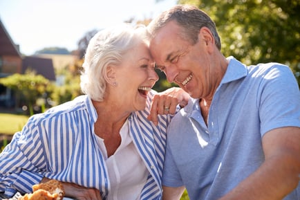 A couple laughs and leans in close together outdoors on a sunny day, capturing the joyful and vibrant lifestyle at our senior living community in Gambrills, MD.