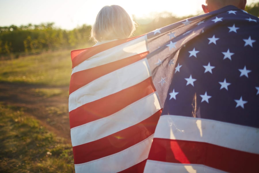 An older adult holds an American flag open in a sunny, open field at golden hour, evoking the proud, spirited lifestyle of active senior living Herndon VA at Arbor Terrace Herndon, a welcoming retirement community Herndon VA.