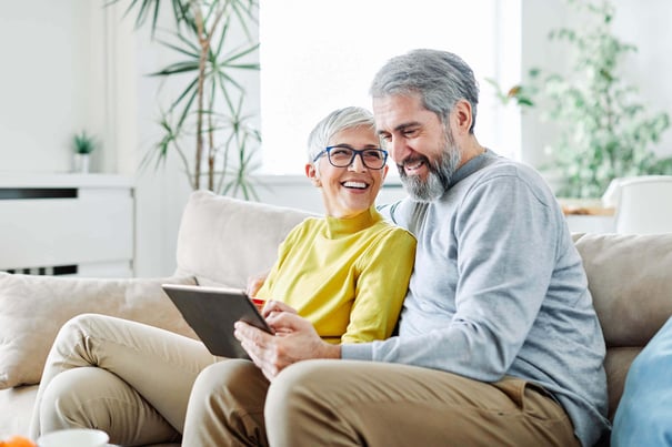 a senior couple sitting on a sofa and browsing a tablet