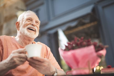 A cheerful older adult holds a cup and laughs outdoors near potted flowers — capturing the joy of touring a senior living community Lakeway TX.