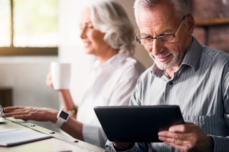 a senior lady enjoying her coffee while a senior man uses an ipad