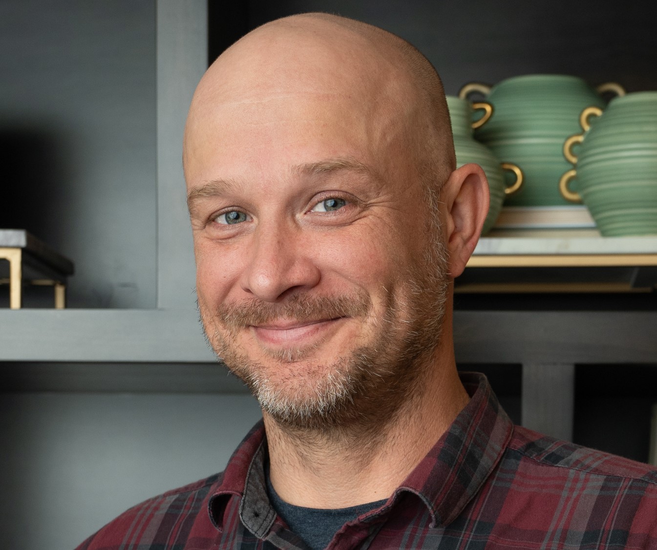Brett McCollum, Maintenance Director at Arbor Terrace Highland Park, smiles in a plaid shirt in front of shelves with green pottery, keeping spaces comfortable at one of the top senior living communities Lake County IL and supporting an active senior lifestyle Highland Park IL.