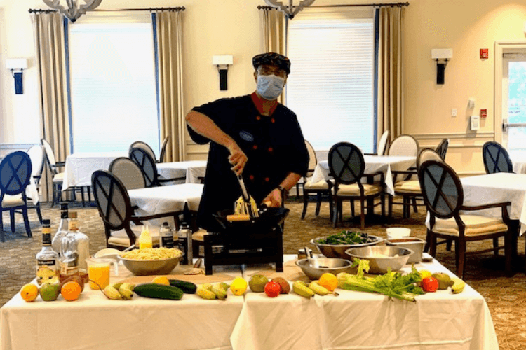 A chef prepares fresh ingredients during a lively cooking demonstration in the elegant dining room, highlighting the inviting dining experience at senior living in Citrus Park, FL.