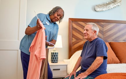 Staff memember Assisting man with attire while he sits on the bed