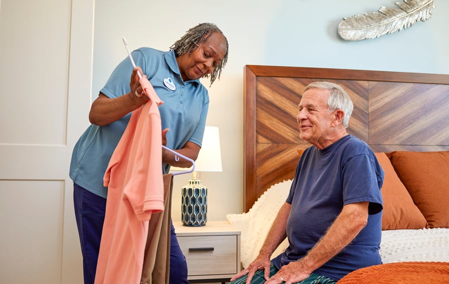 Staff memember Assisting man with attire while he sits on the bed