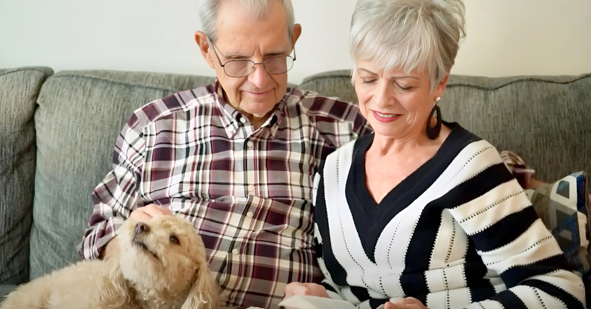 A couple relaxes on a cozy sofa with their small fluffy dog, reflecting the warm, pet-friendly senior living in Citrus Park, FL.