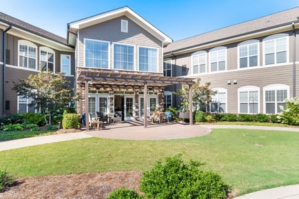 Inviting outdoor patio with a pergola, seating, and lush green lawn at a wellness-focused senior living community in Suwanee, GA, perfect for enjoying fresh air and nature.