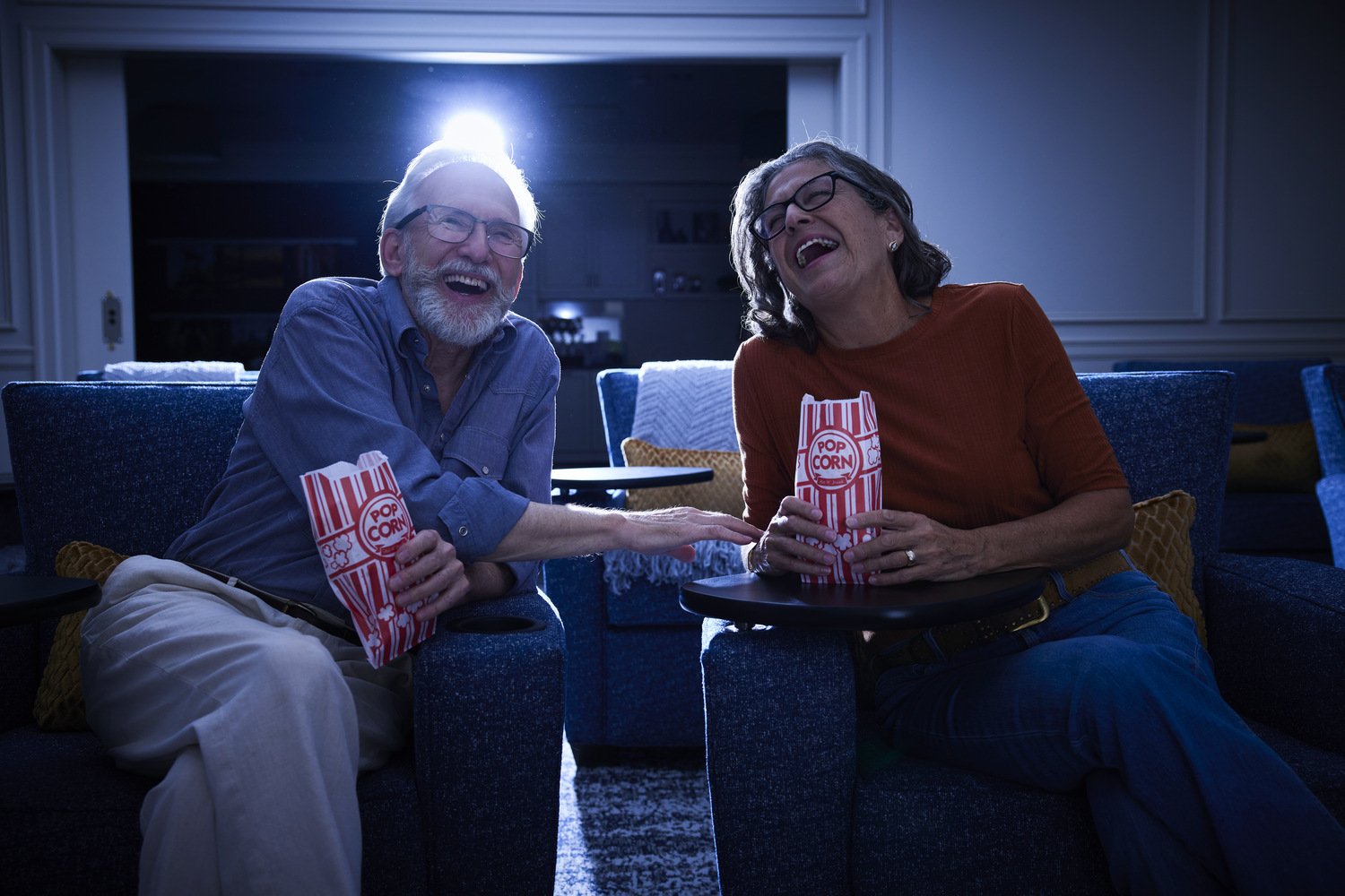 Couple watching a movie in blue chairs with popcorn in hand