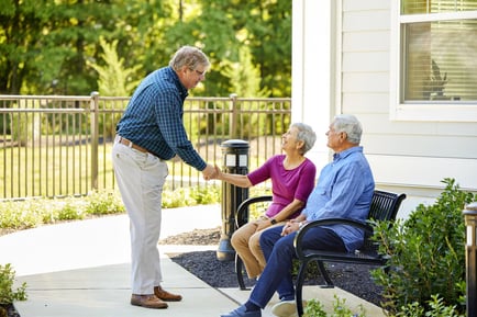 Residents greet each other warmly on a beautifully landscaped outdoor patio, reflecting the friendly, welcoming atmosphere of our senior living community in Gambrills, MD.