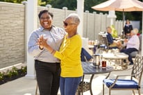 Staff member and resident dancing outside at the patio area with a round table and residents under an umbrella in the background