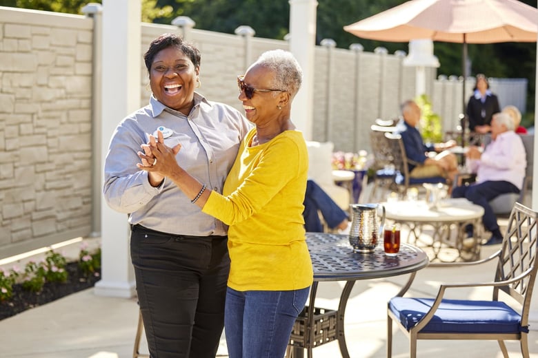 Staff member and resident dancing outside at the patio area with a round table and residents under an umbrella in the background