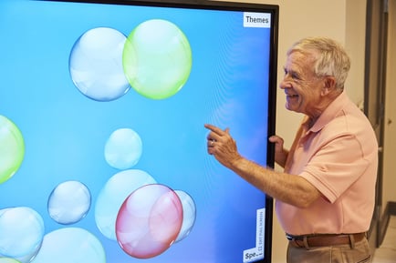 An older adult smiles with delight while interacting with a colorful touchscreen display, showcasing the innovative, engaging activities that define active senior living Herndon VA and the vibrant independent senior lifestyle Herndon VA at Arbor Terrace Herndon