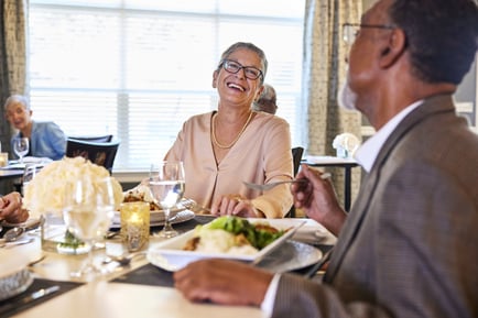 A resident shares a joyful meal and conversation at a beautifully set table, reflecting the gourmet dining and warmth of Glenview senior living.