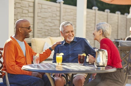 Three residents laugh and share drinks together on a sunny outdoor patio, reflecting the warm, welcoming lifestyle at our senior living community in Gambrills, MD.