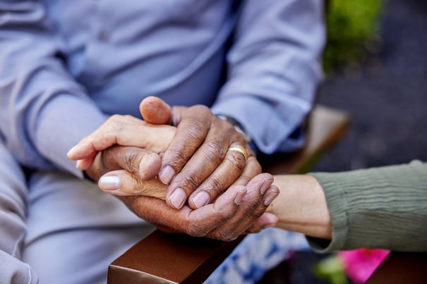 Two pairs of hands rest together in a tender moment outdoors, reflecting the compassionate, person-centered memory care and heartfelt support offered at Arbor Terrace Morris Plains, NJ.