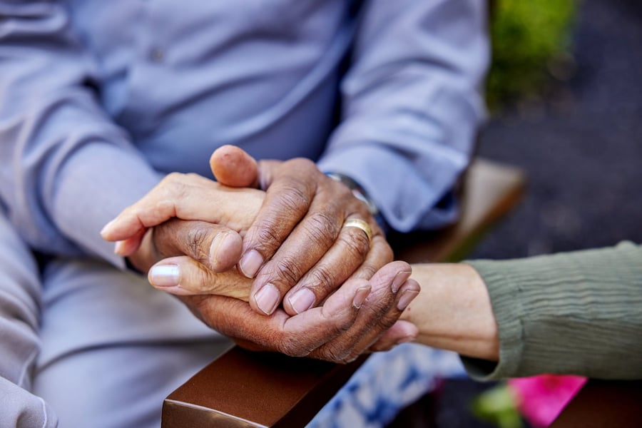 Two pairs of hands rest together in a tender moment outdoors, reflecting the compassionate, person-centered memory care and heartfelt support offered at Arbor Terrace Morris Plains, NJ.