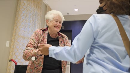 A smiling resident greets a staff member in a sunlit hallway, reflecting the caring North Shore senior living experience in Glenview, IL.