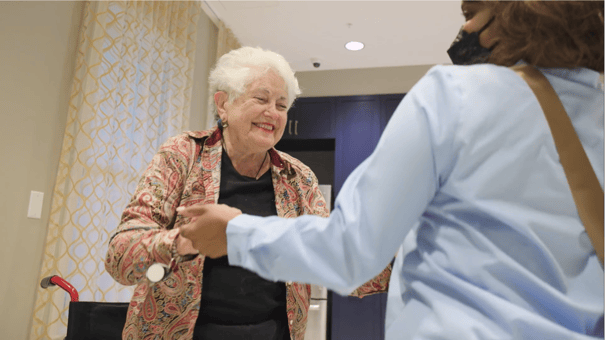 A smiling resident greets a staff member in a sunlit hallway, reflecting the caring North Shore senior living experience in Glenview, IL.