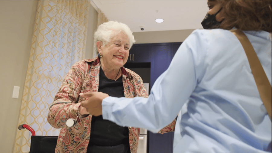 A smiling resident greets a staff member in a sunlit hallway, reflecting the caring North Shore senior living experience in Glenview, IL.