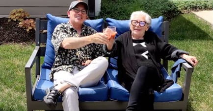 Two men share a laugh and a toast on a cozy outdoor sofa, reflecting the active senior lifestyle and outdoor amenities at Arbor Terrace Glenview.