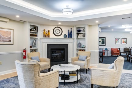 A welcoming common area lounge with a classic fireplace, built-in shelving, and comfortable armchairs at Arbor Terrace Herndon, showcasing the warm, resort-style independent living Herndon atmosphere of this distinguished senior living Herndon Virginia community