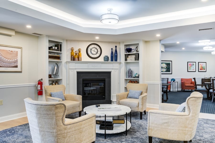 A welcoming common area lounge with a classic fireplace, built-in shelving, and comfortable armchairs at Arbor Terrace Herndon, showcasing the warm, resort-style independent living Herndon atmosphere of this distinguished senior living Herndon Virginia community