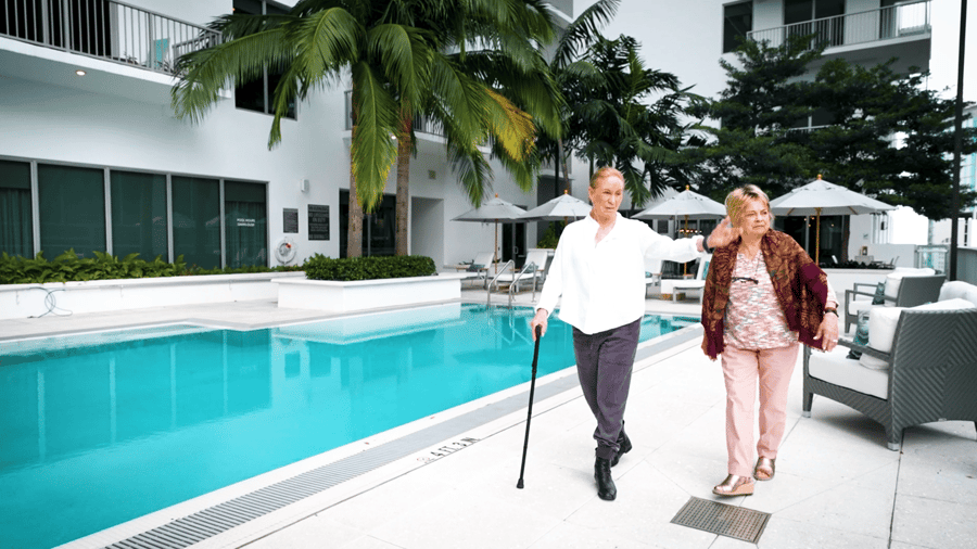Two women stroll together along the poolside at Mirabelle in Miami, FL, where the full continuum of senior care supports residents at every stage with personalized attention and beautiful surroundings.