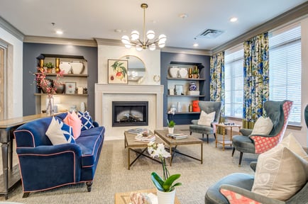 A beautifully appointed sitting room features a fireplace, elegant chandelier, navy blue sofas, and colorful accent chairs, reflecting the upscale, welcoming atmosphere of our senior living East Cobb and assisted living Marietta GA community.
