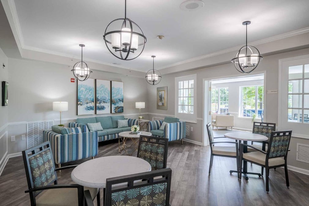 dining space with wooden floors, white walls, pendant chandeliers, wide windows, white double doors, and round tables with dining chairs