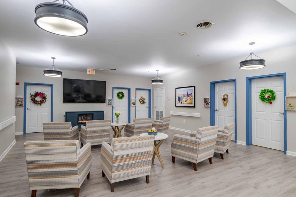 Entertainment area with a mounted television at the middle with a fireplace underneath. Arm chairs and coffee tables around. 