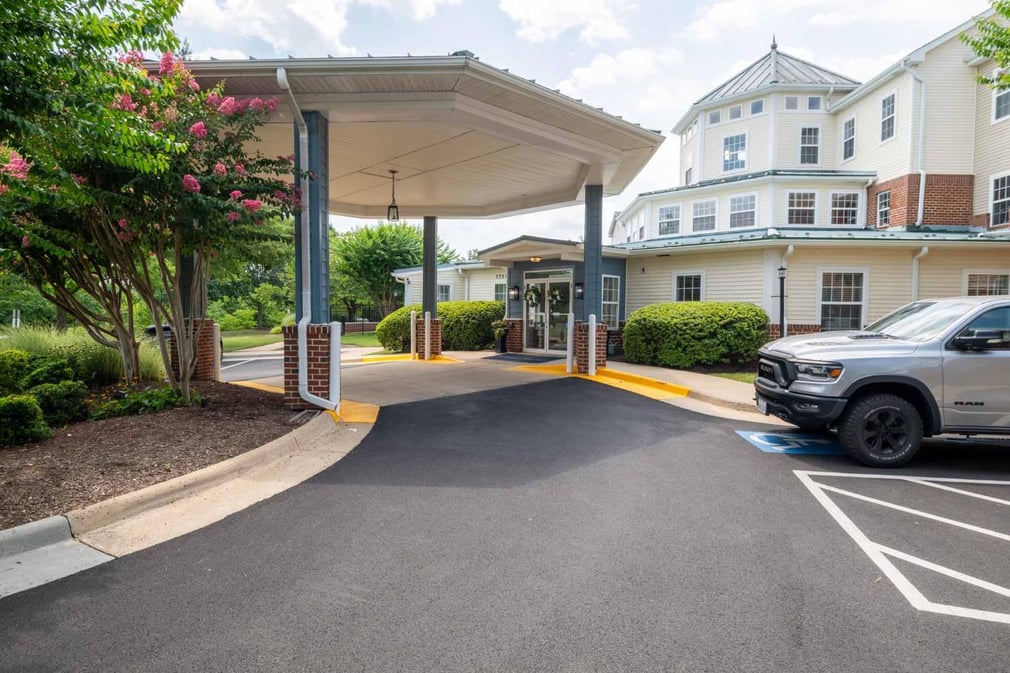 asphalt road leading to front entrance of white building with a covered entrance way, car parked at the side