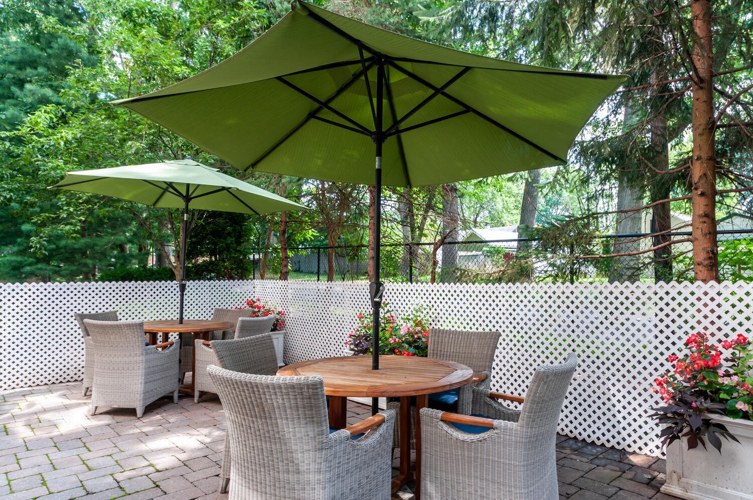 Arbor Terrace Teaneck patio area with grey wicker chairs and a wooden tables with green umbrellas.