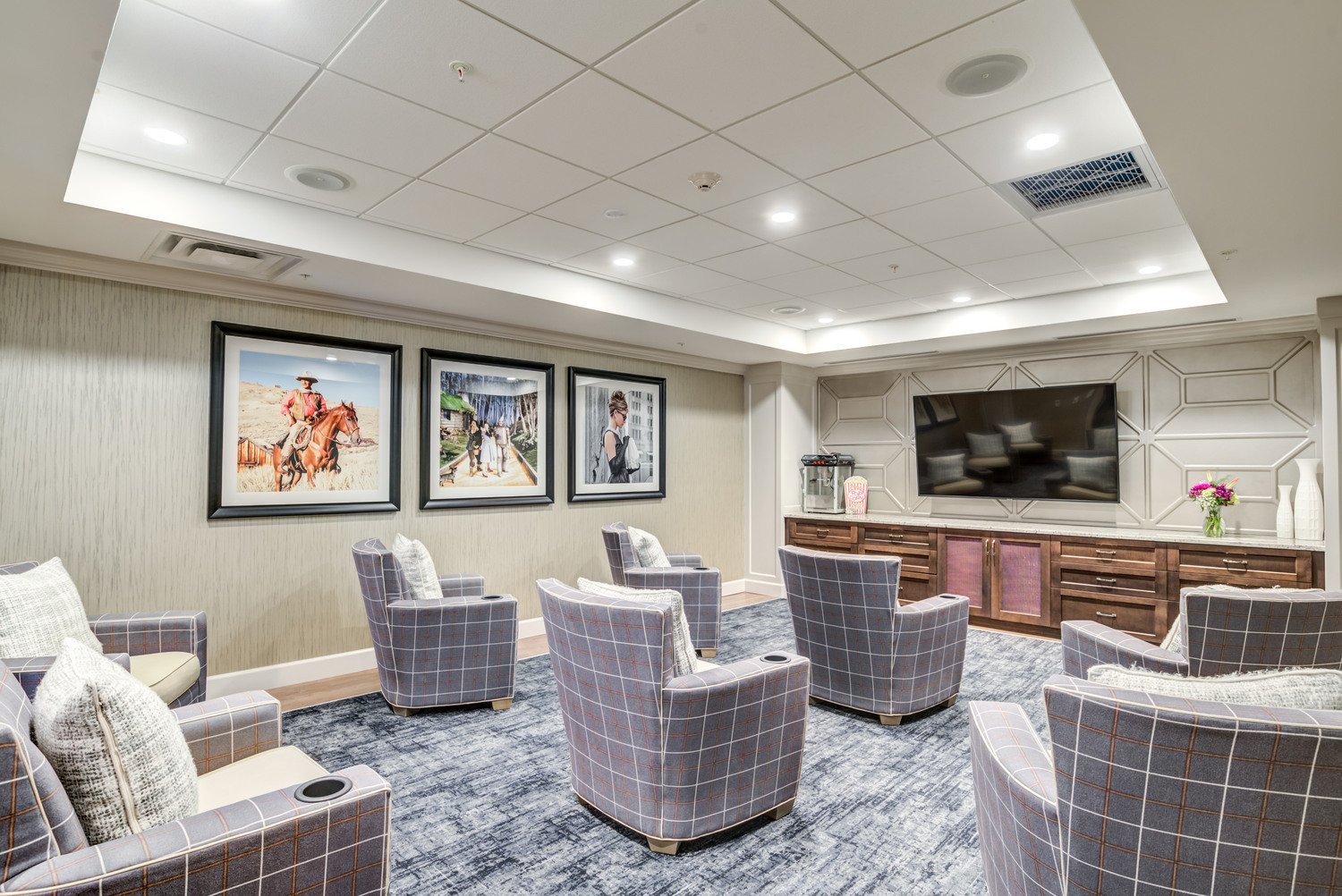 movie theater area with grey and white striped chairs and cupholders. picture frames in the background and a popcorn machine and big tv