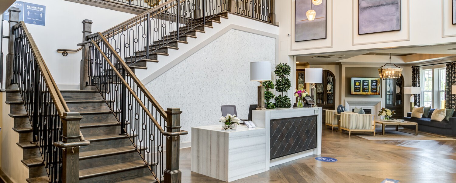 Lobby area with a wooden grand staircase. White front desk and wooden floors