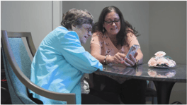 A senior lady and a staff member looking through a phone together while sitting down. 