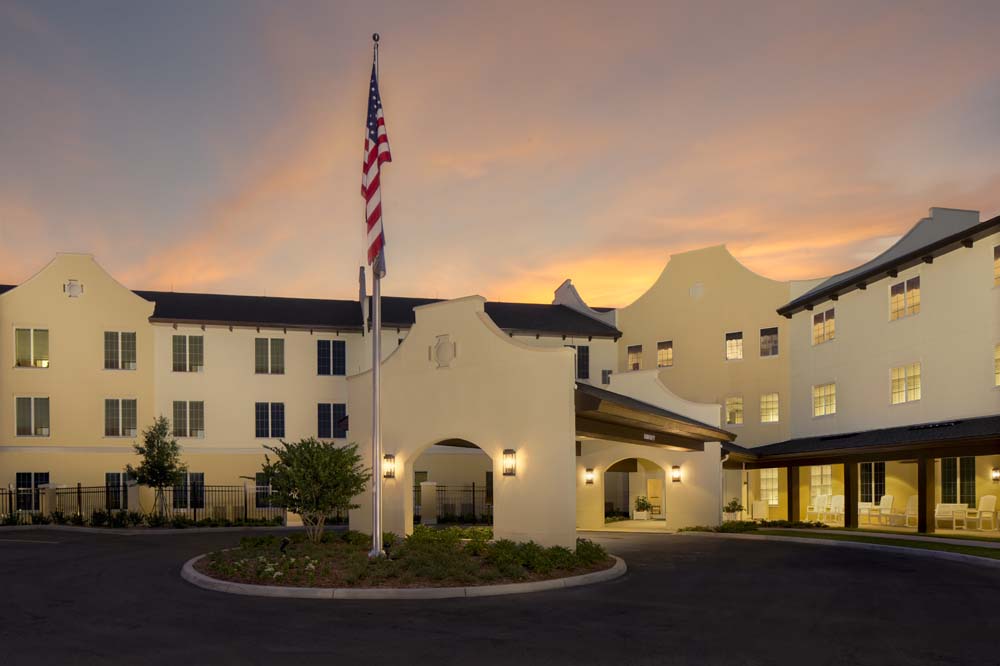 The welcoming exterior of the community building glows warmly at sunset beneath an American flag, showcasing the inviting atmosphere of senior living in Citrus Park, FL.