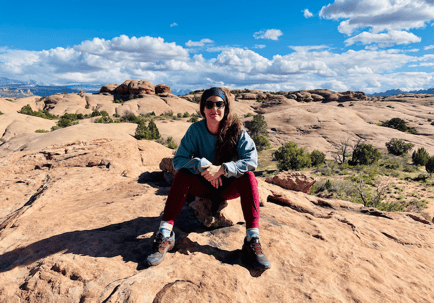 A staff member sits on rocky desert terrain under a bright blue sky — reflecting the adventurous spirit behind the dedicated senior care team at Arbor Terrace Lakeway TX.