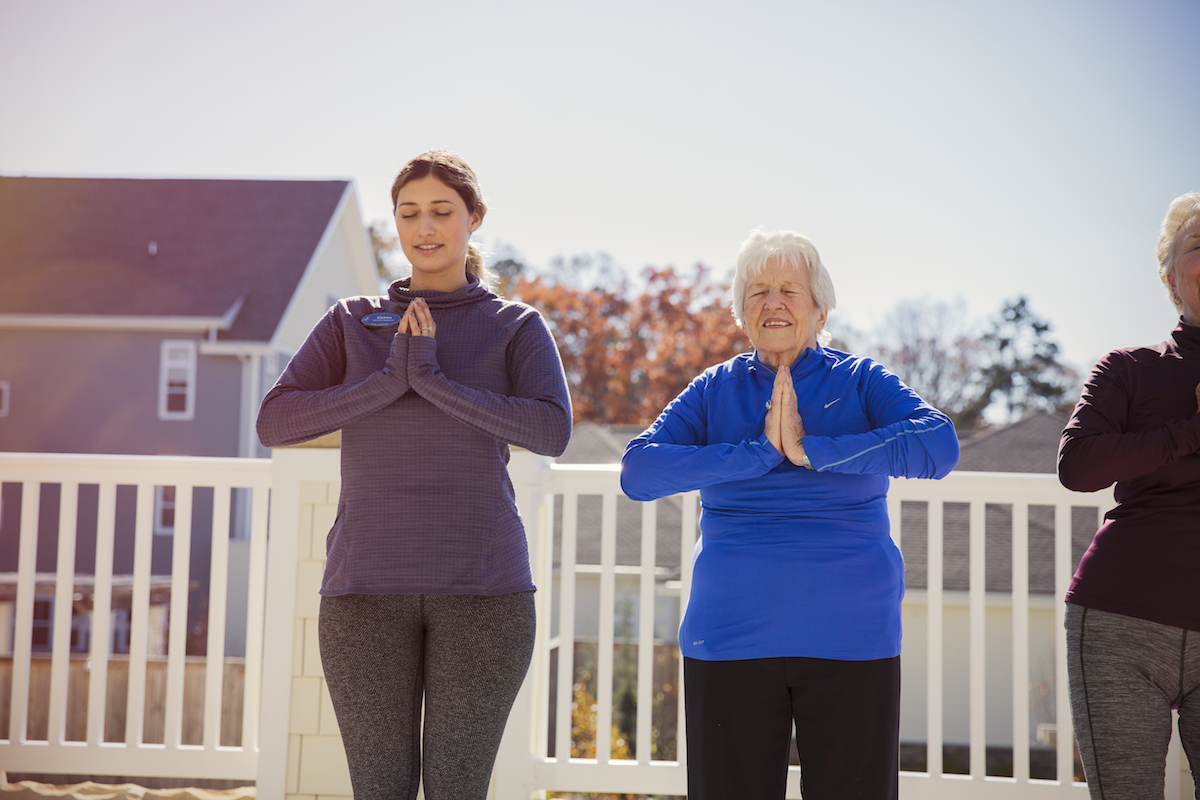 A resident practices a peaceful yoga pose alongside a staff instructor on a sunny outdoor deck, reflecting the active senior living in Citrus Park, FL.