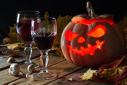 A glowing carved jack-o-lantern sits beside two glasses of red wine on a rustic table, capturing the festive Halloween spirit at our senior living community in Gambrills, MD.