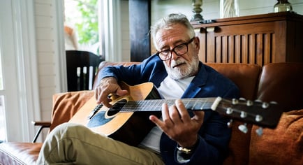 A resident relaxes on a leather sofa while playing acoustic guitar, enjoying the enriching and engaging senior living lifestyle at our community in Gambrills, MD.