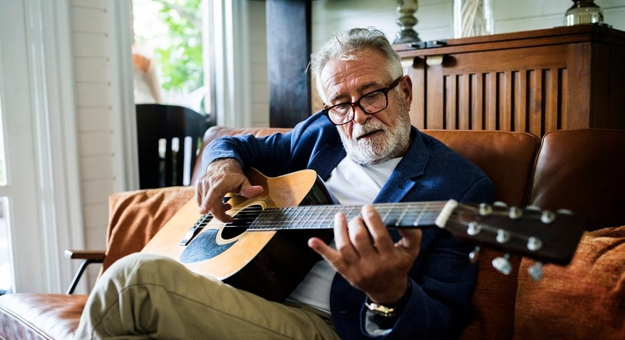 A resident relaxes on a leather sofa while playing acoustic guitar, enjoying the enriching and engaging senior living lifestyle at our community in Gambrills, MD.