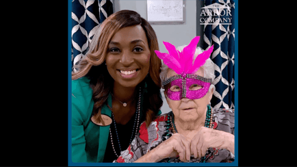 A staff member and a resident pose together wearing colorful Mardi Gras beads and a festive feathered mask, highlighting the fun, spirited celebrations that make our senior living East Cobb and assisted living Marietta GA community so special.