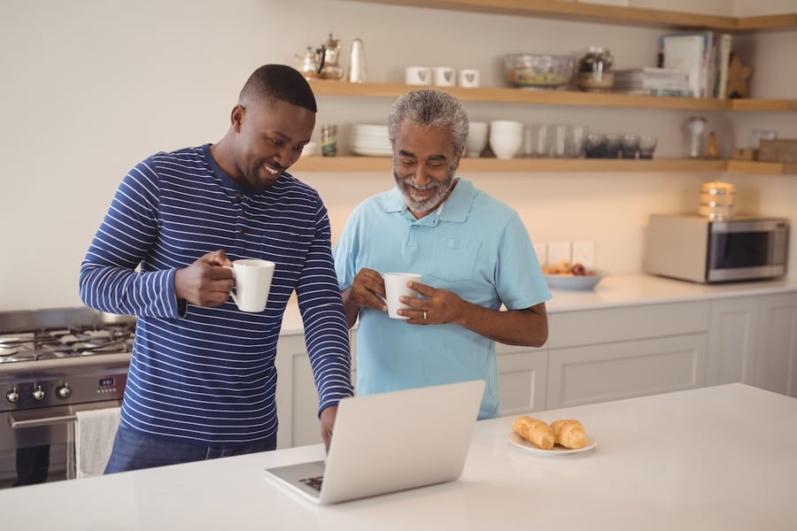 a senior man and son use a laptop while drinking coffee in the kitchen