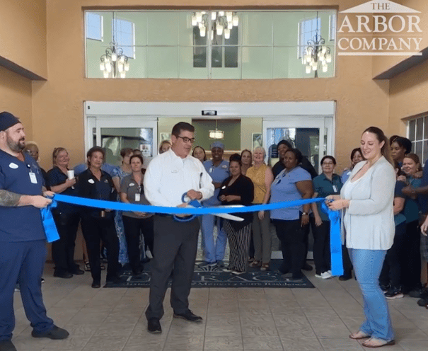 A large group of staff members gathers at the front entrance of Barrington Terrace of Fort Myers, FL, for a ribbon-cutting ceremony celebrating the community's grand reopening.
