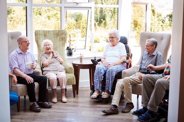 A group of seniors laugh and enjoy each other's company in a bright, sunlit sitting area, reflecting the welcoming social atmosphere of assisted living in Mountainside, NJ.