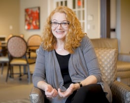 A staff member at Arbor Terrace Glenview senior living smiles warmly while seated in the community lounge, reflecting senior living with wellness programs Glenview IL.