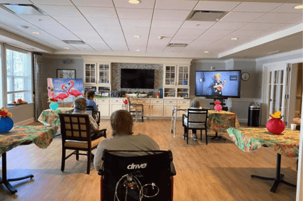 Residents enjoy a lively virtual entertainment event in a festively decorated activity room at Arbor Terrace Morris Plains, showcasing the engaging, activity-rich memory care and assisted living programs in Morris Plains, NJ.
