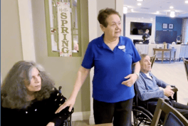 A staff member chatting with residents near a spring-themed wall sign at Arbor Terrace Highland Park, a senior living community in Highland Park, IL.